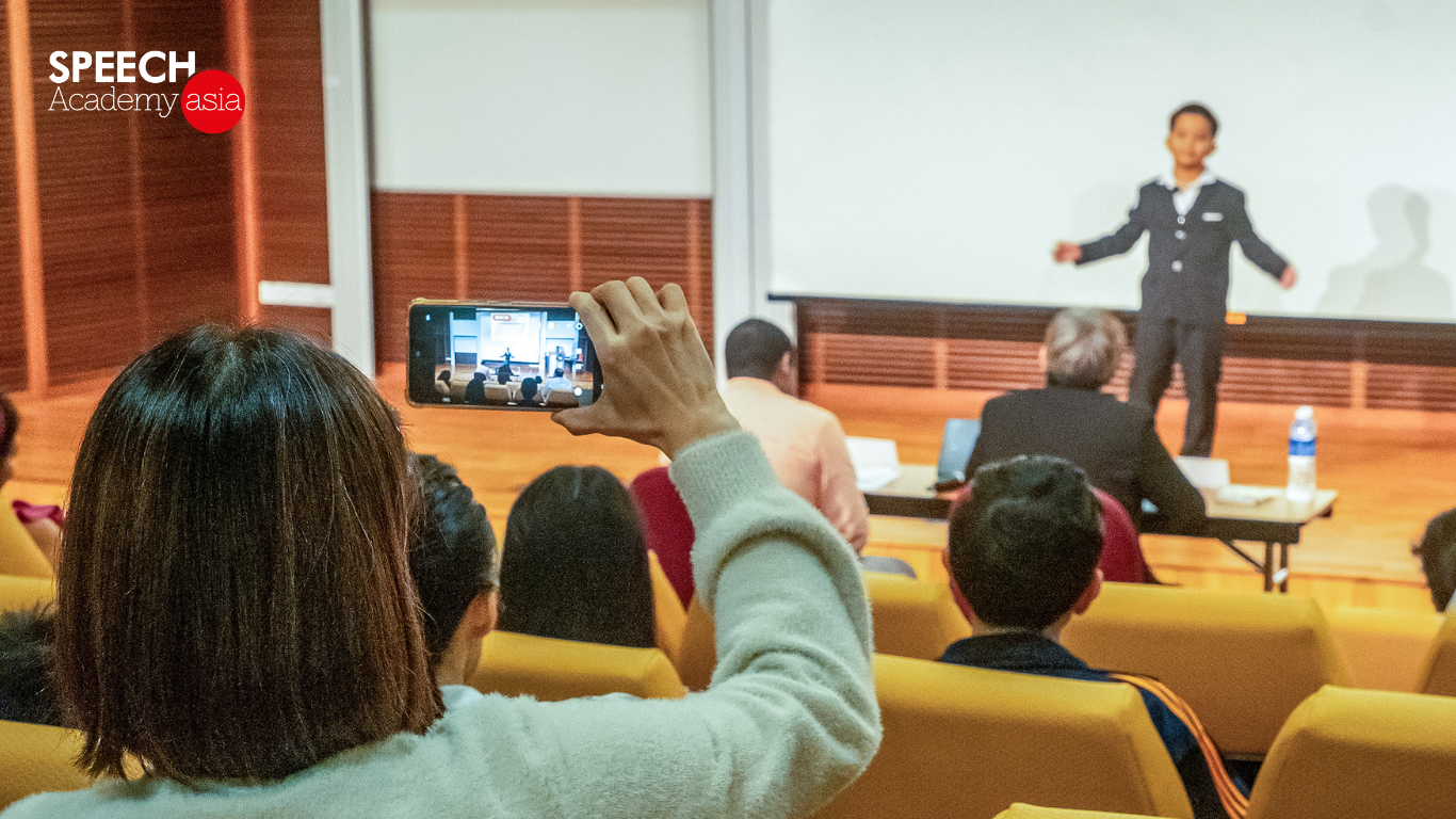 A child confidently delivering a public speech on stage in front of an audience.