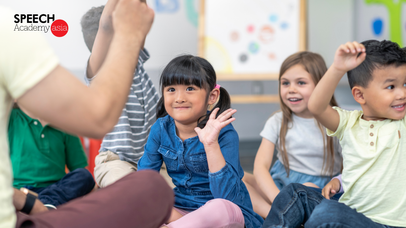 Students in a classroom during a communications skills lesson, with one child raising their hand to answer a question
