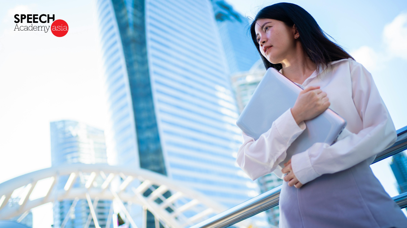 Confident woman presenting a laptop during a speaking with confidence course in Singapore with high rise buildings in the background
