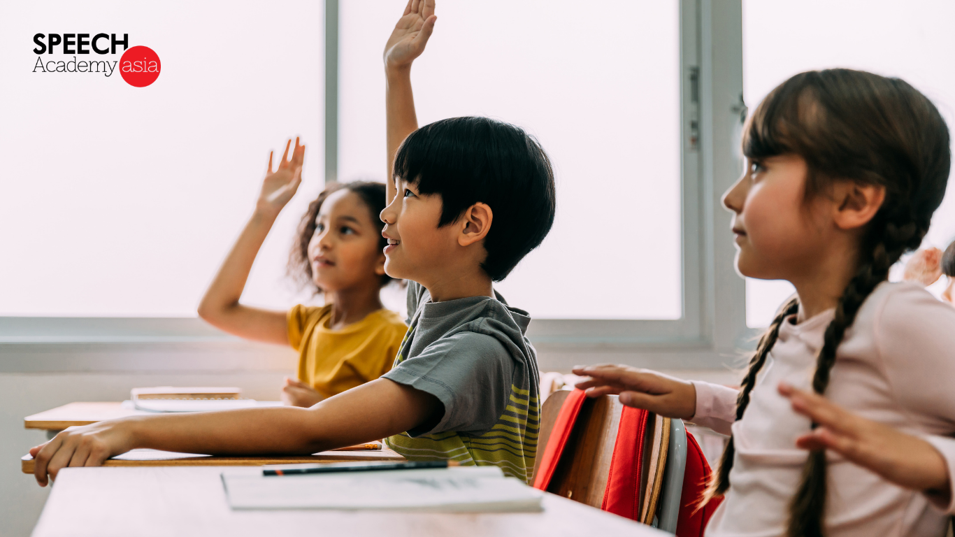 Three students participating in a public speaking class, with one student raising his hand to answer a question.